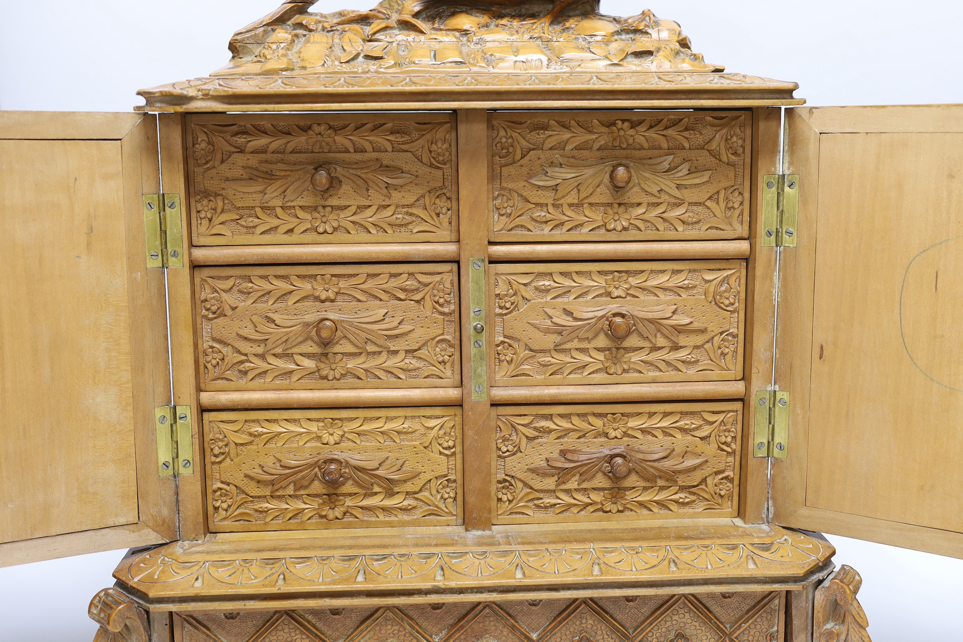 A late 19th century Black Forest carved wooden two door table top cabinet, interior with fitted drawers, surmounted with two pheasants, 51cm high
